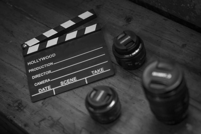 Black and white photograph of a clapperboard and camera equipment on a table.
